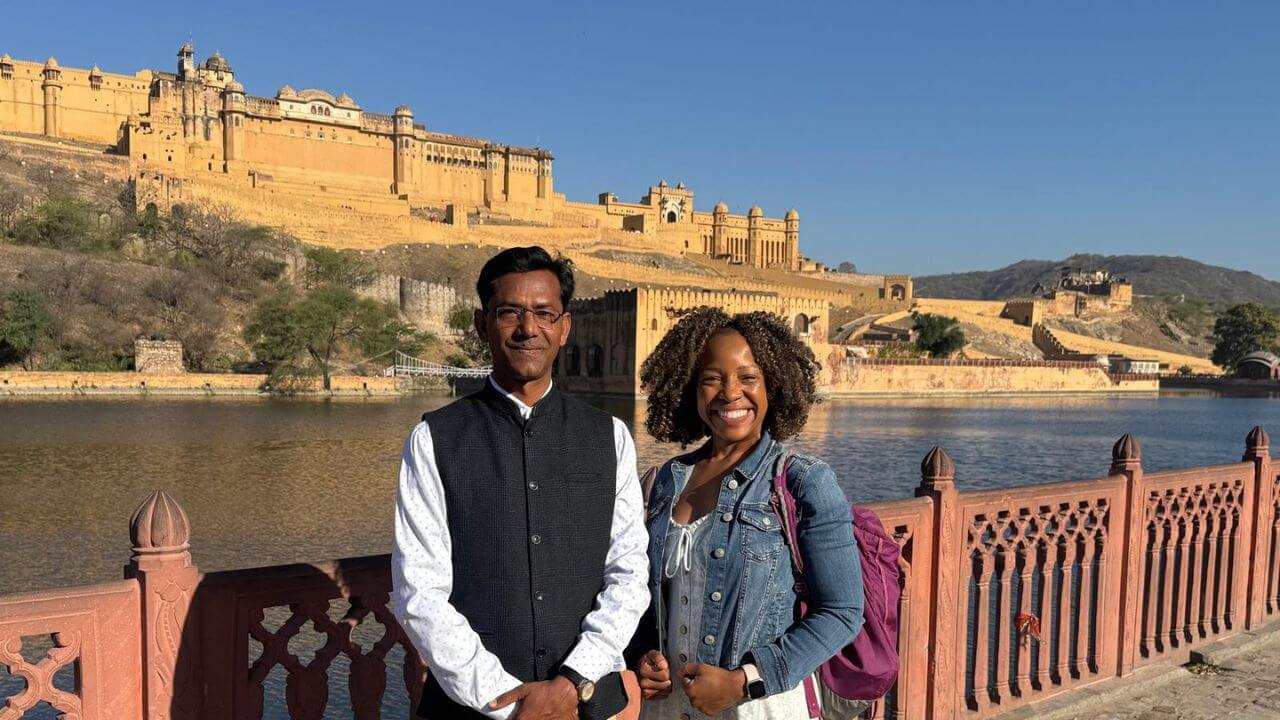Two tourists standing beside Maota Lake with Amber Fort in the background during the Jaipur 2 Days 1 Night Tour.