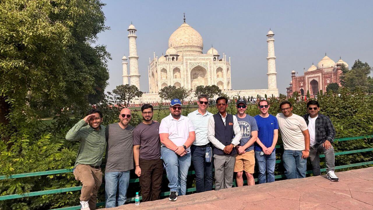 A group of tourists posing in front of the Taj Mahal during a luxury day tour from Delhi, with their guide standing beside them.