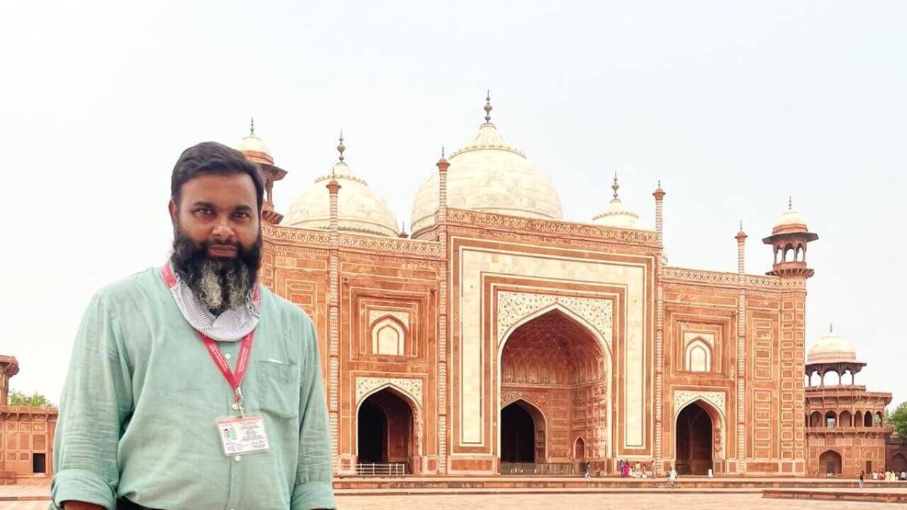 A tour guide with an official badge stands in the courtyard beside the Taj Mahal mosque in Agra, India, captured during the 6 Days Golden Triangle With Tiger Safari tour.