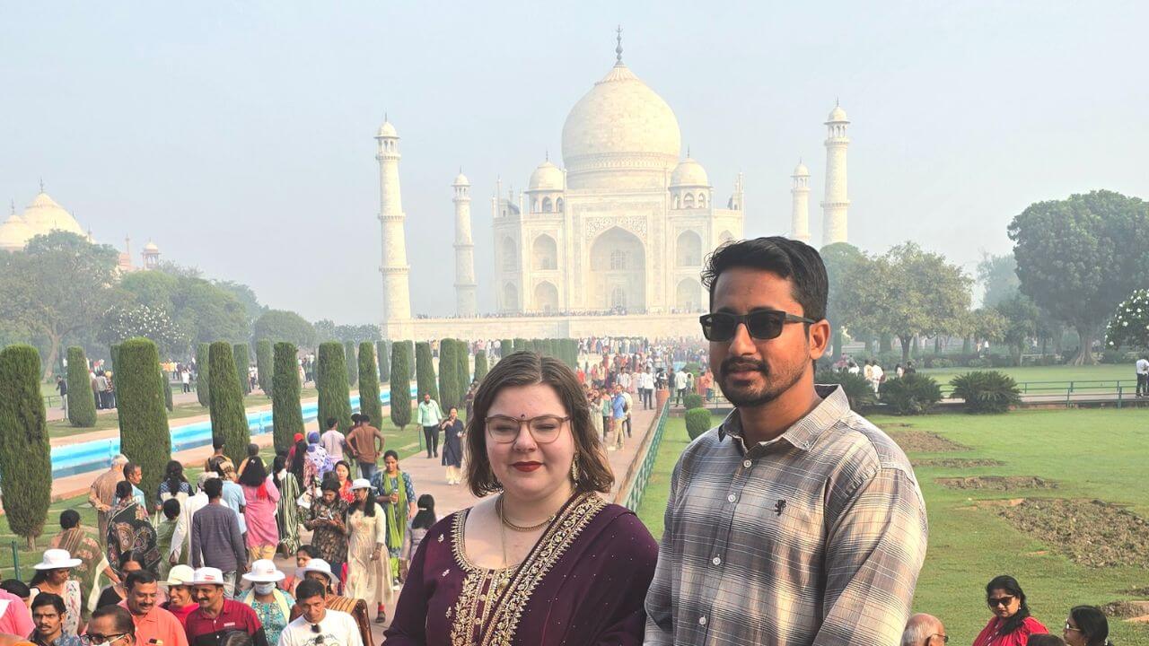 Two tourists standing in front of the Taj Mahal during the Overnight Taj Mahal Tour from Delhi by Train, surrounded by morning crowds in Agra.