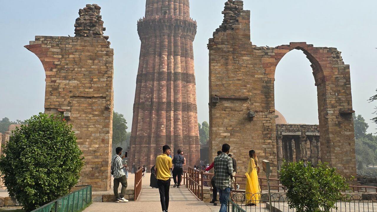 Tourists walking toward Qutub Minar through the stone arch ruins during the Old and New Delhi with Golden Temple Tour.