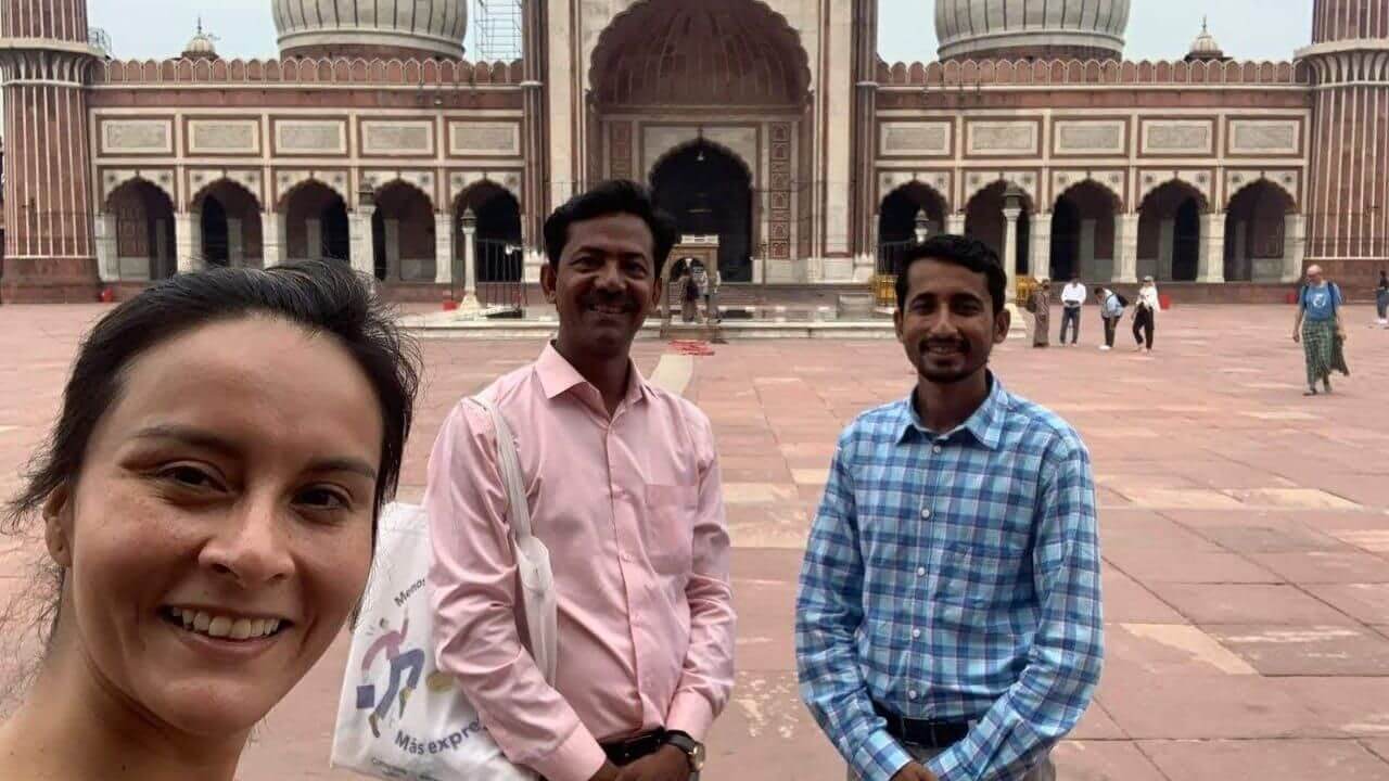 Three travelers smiling in the courtyard of Jama Masjid in Delhi during the Golden Triangle Tour, with the mosque’s domes and archway visible in the background.